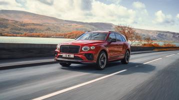 Bentley Bentayga S in Orange Flame - by Mulliner featuring black matrix upper and lower grille driving along a road. 