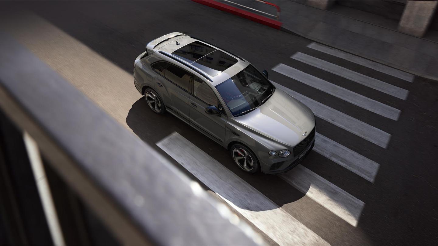 Top view Bentley Bentayga S in Cambrian Grey paint with sunroof in view driving through a zebra crossing.