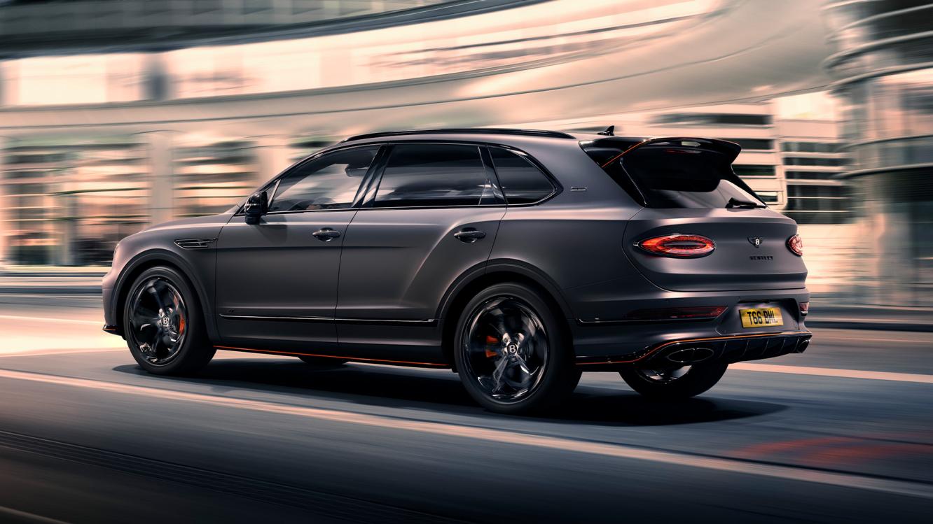 Bentley Bentayga S Black Edition driving dynamically through a city featuring 22 inch S directional wheel - Black Painted and Polished as well as Mandarin accents on the styling kit