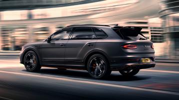 Bentley Bentayga S Black Edition driving dynamically through a city featuring 22 inch S directional wheel - Black Painted and Polished as well as Mandarin accents on the styling kit