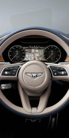 Close up on Bentley Continental GT Azure's Heated, Duo-Tone Linen and Beluga hide, 3 Spoke, Hide Trimmed Steering Wheel with dashboard gauges in view.