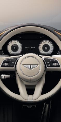 Close up on Bentley Continental GT Mulliner's Heated, Duo-Tone Linen and Beluga hide, 3 Spoke, Hide Trimmed Steering Wheel with dashboard gauges in view.