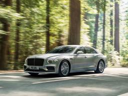 Bentley Flying Spur Signature model, in Moonbeam exterior colour featuing 21 inch Ten Twin Spoke - Painted wheels, diving on road with trees in backdrop.
