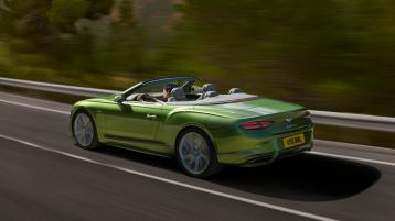Rear side angled view of the new Bentley Continental GT Convertible Speed in Tourmaline Green featuring 21 inch directional and diamond cut Speed wheels driving in a rural environment