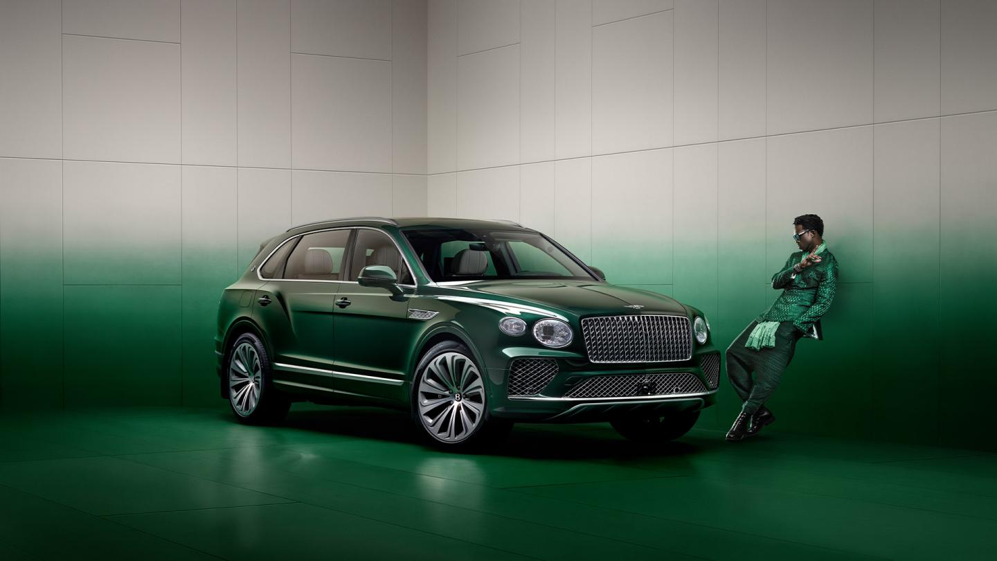 Wisdom Kaye standing next to the front three quarter of the Bentayga Atelier Edition in an Emerald exterior colours with bright chrome accents