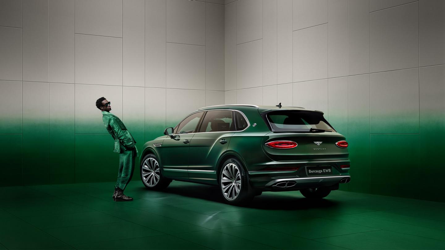Wisdom Kaye standing next to the rear three quarter of the Bentayga Atelier Edition in an Emerald exterior colours with bright chrome accents