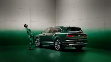 Wisdom Kaye standing next to the rear three quarter of the Bentayga Atelier Edition in an Emerald exterior colours with bright chrome accents