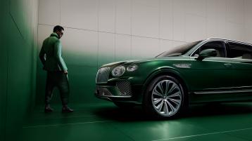 Wisdom Kaye standing next to the front three quarter of the Bentayga Atelier Edition in an Emerald exterior colours with bright chrome accents