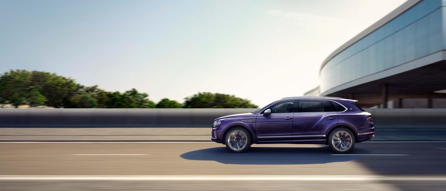 Side angled view of Bentley Bentayga EWB Mulliner in Tanzanite Purple driving along highway.