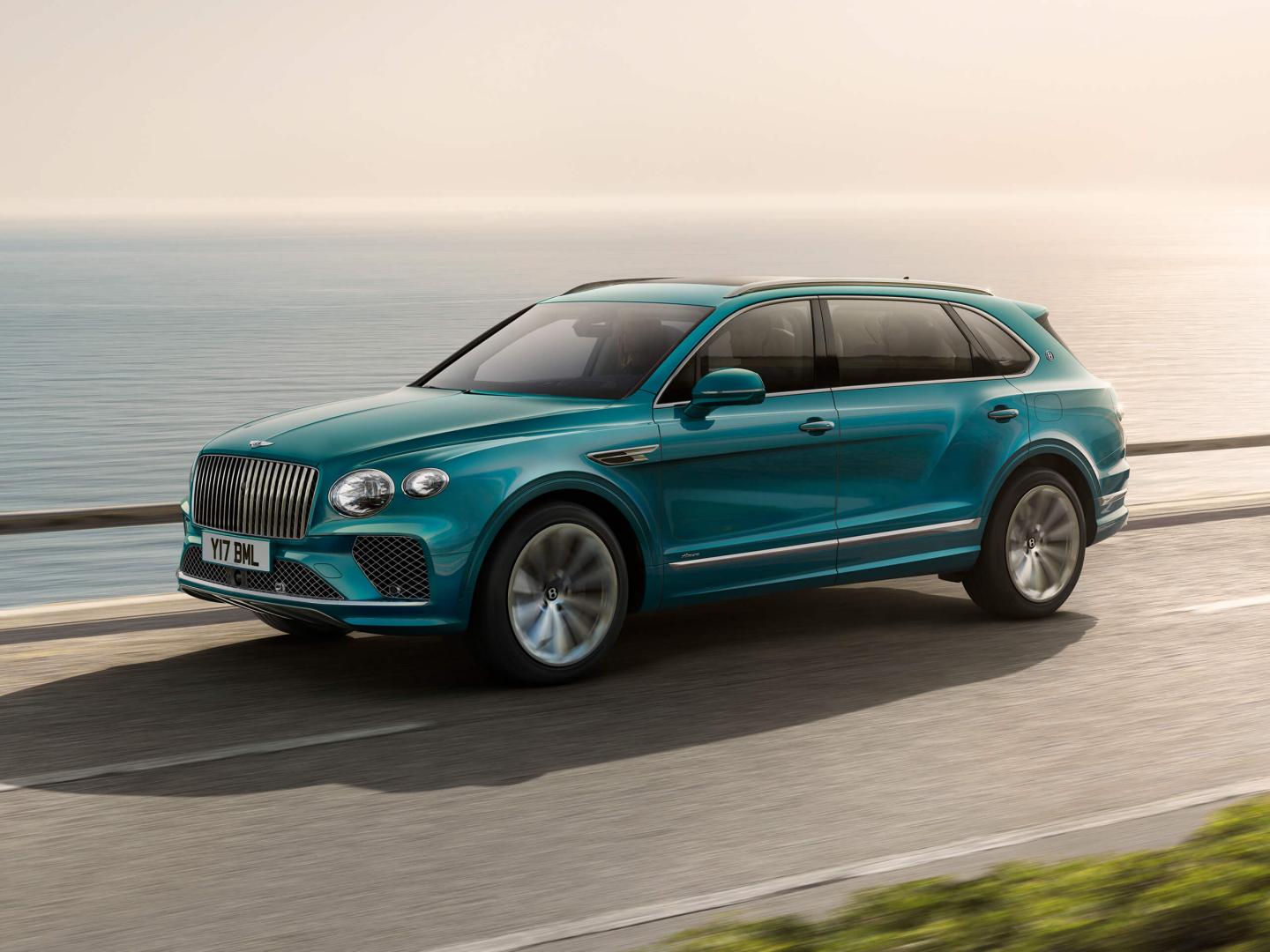 Bentley Bentayga EWB Azure side view in Topaz blue / Kingfisher- by Mulliner colour, featuring 22 inch ten spoke wheel - Painted with chrome accents driving along sea side.