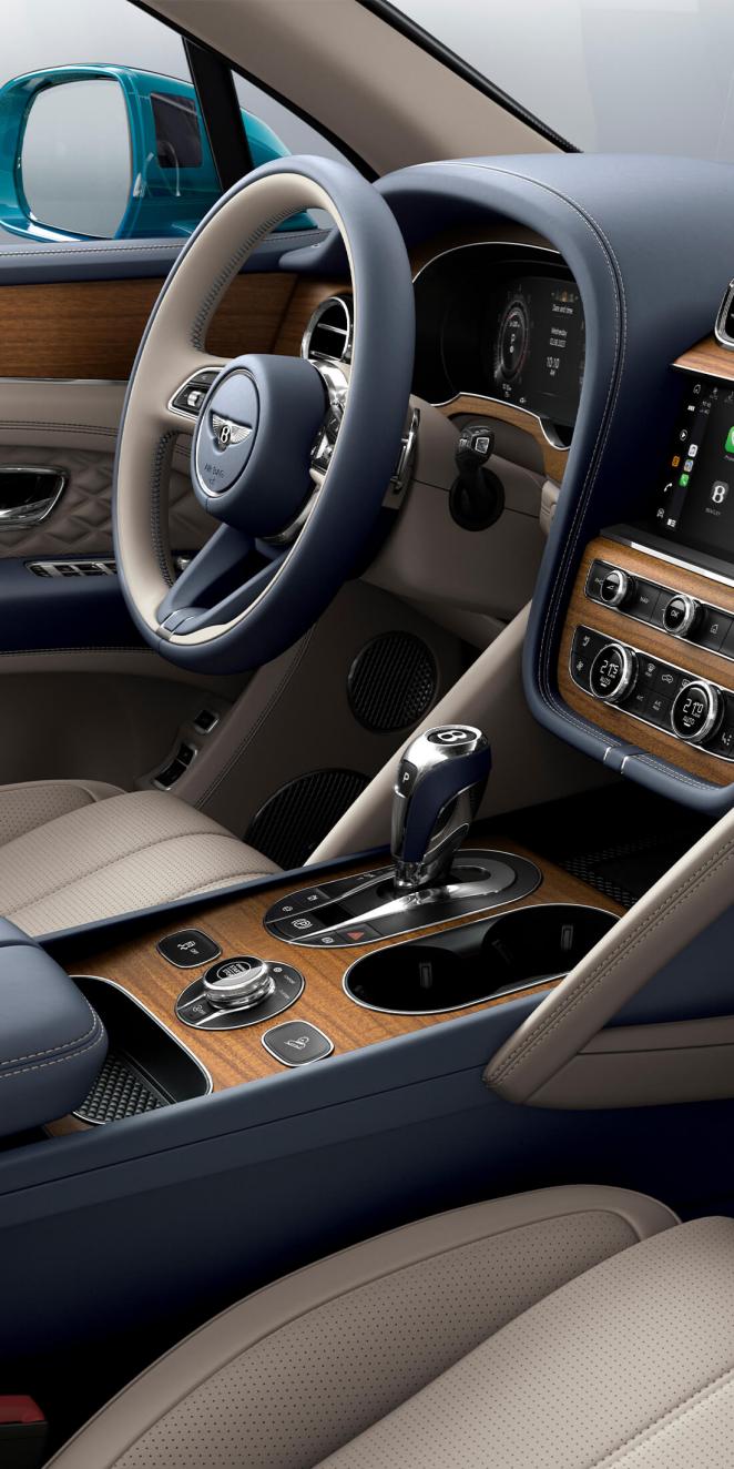 Bentley Bentayga EWB Azure interior with central console set in Open Pore Koa veneer and Portland hide seats, view from the passenger seat over looking the driver's seat. 