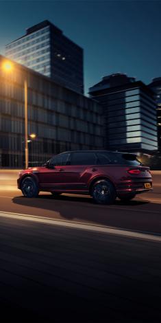 Bentley Bentayga EWB Mulliner with Black Crystal over Cricket Ball exterior paint featuring 22 inch Mulliner Wheel - Black painted, driving in urban area.