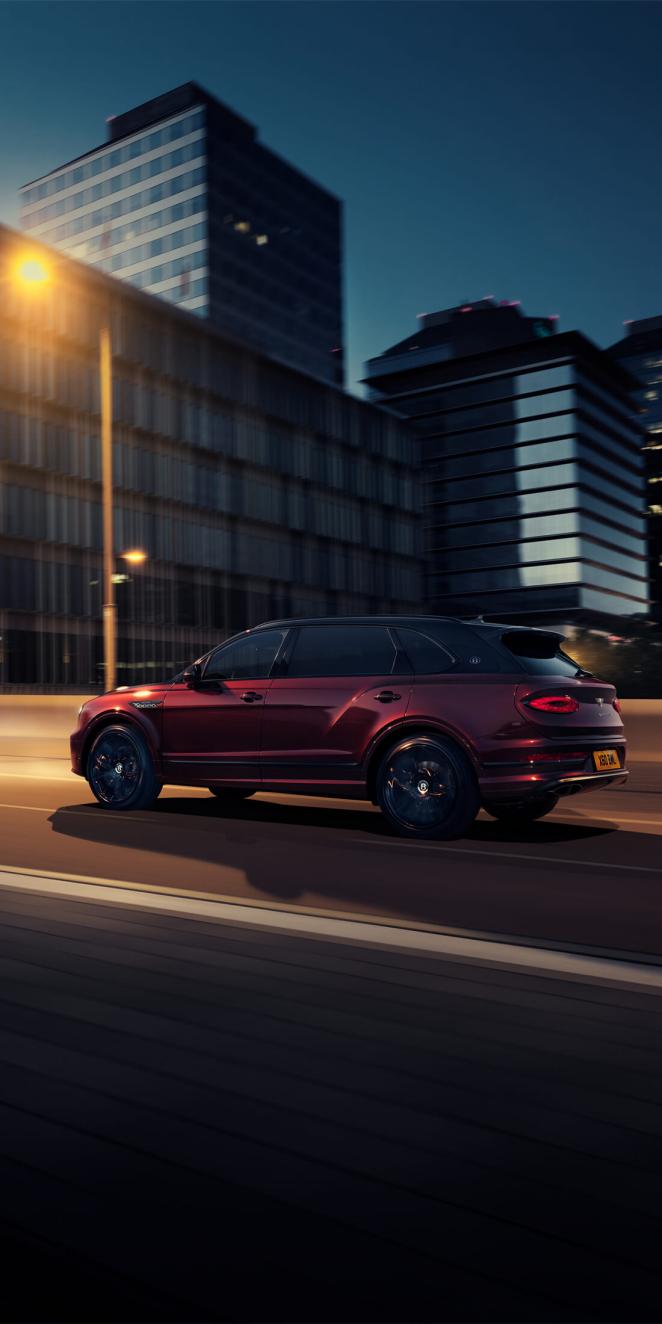 Bentley Bentayga EWB Mulliner with Black Crystal over Cricket Ball exterior paint featuring 22 inch Mulliner Wheel - Black painted, driving in urban area.