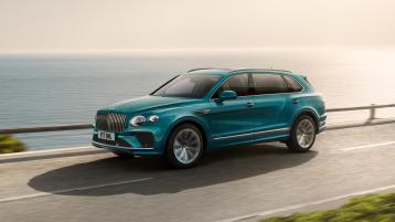 Front side angled view of Bentley Bentayga EWB Azure in Topaz Blue with chrome accent, driving along sea side.
