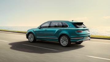 Bentley Bentayga EWB Azure in Topaz Blue colour, rear view with Black painted shark fin aerial and Oval split tailpipe driving along sea side.