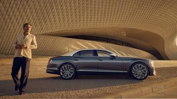 Side profile of the new hybrid Bentley Flying Spur Mulliner in Mulliner Duo Tone exterior colours featuring 22 inch directional and diamond cut wheels driving in a urban environment
