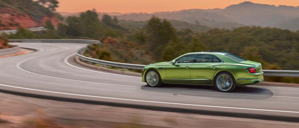 Rear 3/4 of new Bentley Flying Spur speed in Tourmaline Green featuring  Flying ‘B’ radiator mascot – bright polished stainless, driving along a bridge in the mountains