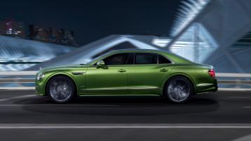Side angled view of new Bentley Flying Spur speed in Tourmaline Green featuring  Flying ‘B’ radiator mascot – bright polished stainless, driving in urban environment