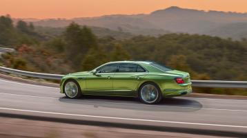 Rear 3/4 of new Bentley Flying Spur speed in Tourmaline Green featuring  Flying ‘B’ radiator mascot – bright polished stainless, driving along a bridge in the mountains