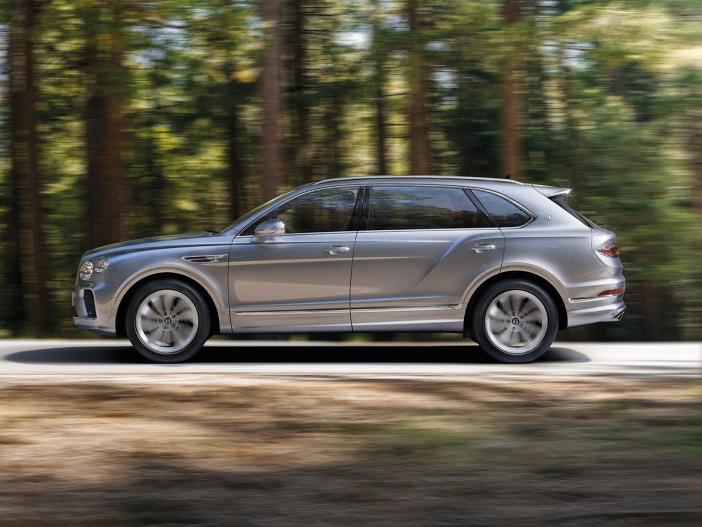 Side view of Bentley Bentayga EWB in Moonbeam colour driving through forest featuring Bentley ‘B’ wing vent.