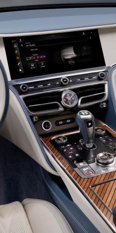 Bentley Flying Spur Azure V8 in Topaz Blue colour with chrome accents and featuring 22 inch ten spoke wheels - black painted and machined, driving along a seaside road.