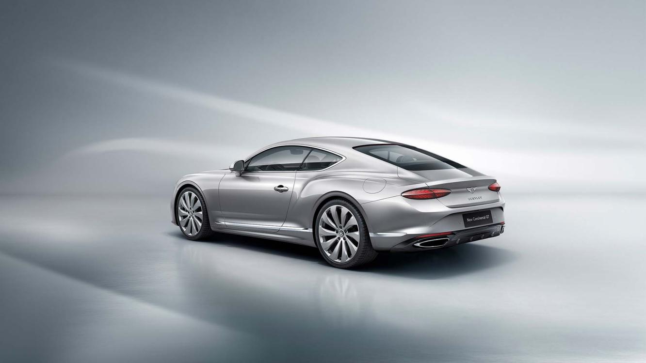 Rear three quarter of the new hybrid Bentley Continental GT in a Moonbeam exterior featuring 22" directional wheels driving in a rural environment