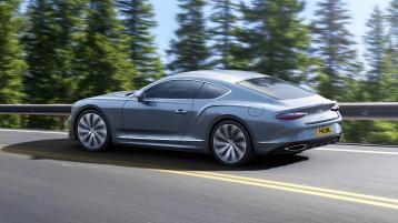 Rear three quarter of the new hybrid Bentley Continental GT in a Moonbeam exterior featuring 22" directional wheels driving in a rural environment