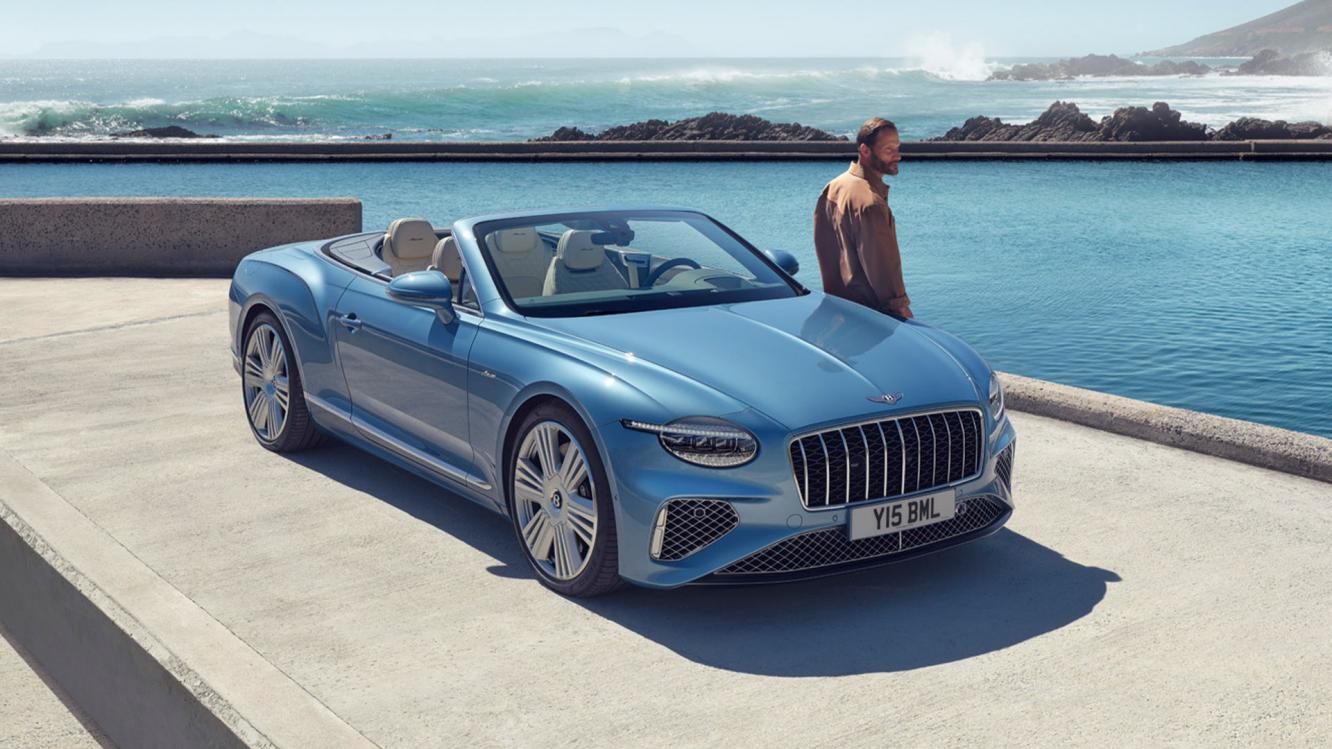 Front side angled view of Continental GTC Azure in Light Windsor Blue driving by the sea