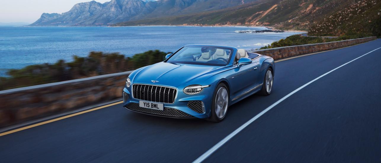 Front side angled view of Continental GTC Azure in Light Windsor Blue driving by the sea