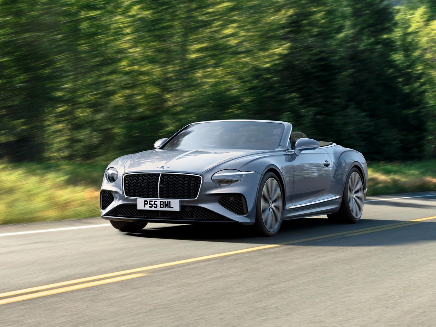 Bentley Continental GTC Signature model in Moonbeam colour featuring Black gloss matrix grille with chrome surround, driving with greenery in backdrop.