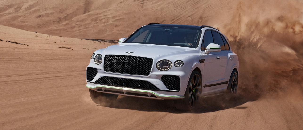New Bentayga Speed in Snow Quartz by Mulliner exterior paint with the Bentayga Styling Specification and 23" Directional Wheels driving on sand dunes.