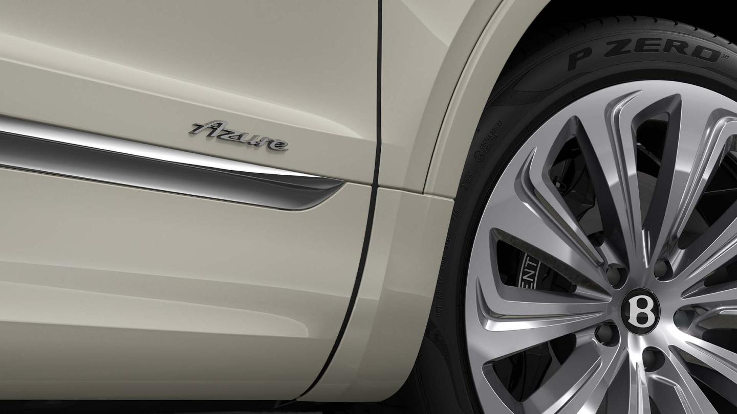  Side skirt view of Bentley Bentayga Azure in White Sand with chome accents and Azure exterior door badge in focus with 22" Ten Spoke Wheel.