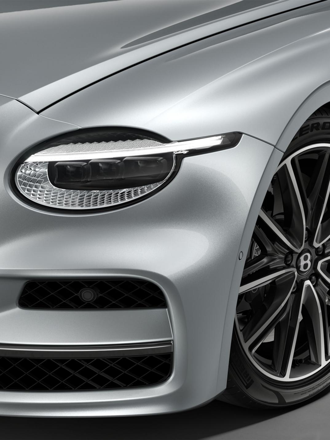 Front three-quarter close-up of the Bentley Flying Spur in Moonbeam showing the headlights and 21" Ten Twin Spoke Wheel in Dark Grey Painted and Bright Machined finish.