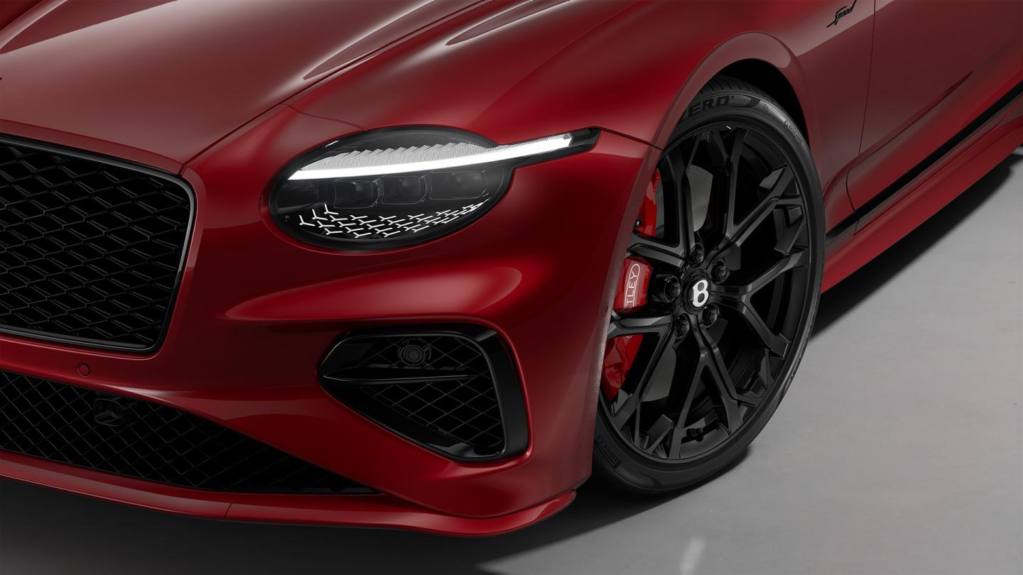 Close‑up of the headlights on the Bentley Continental GT Speed in Candy Red, shown with 22‑inch Ten‑Spoke Sports Wheels in black.