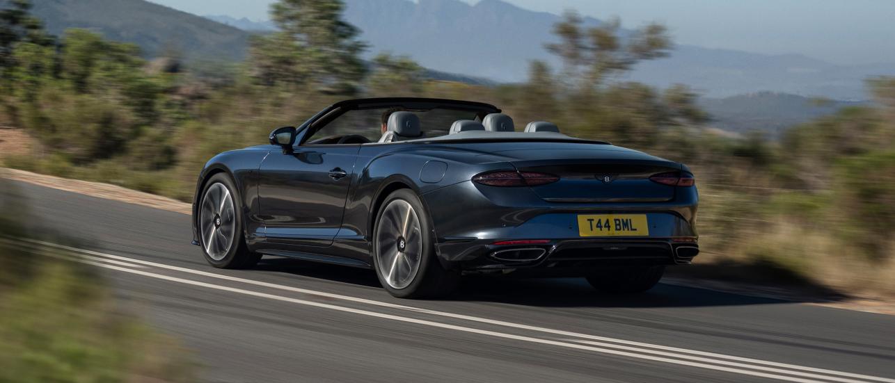 Front side angled view of Continental GTC Azure in Light Windsor Blue driving by the sea