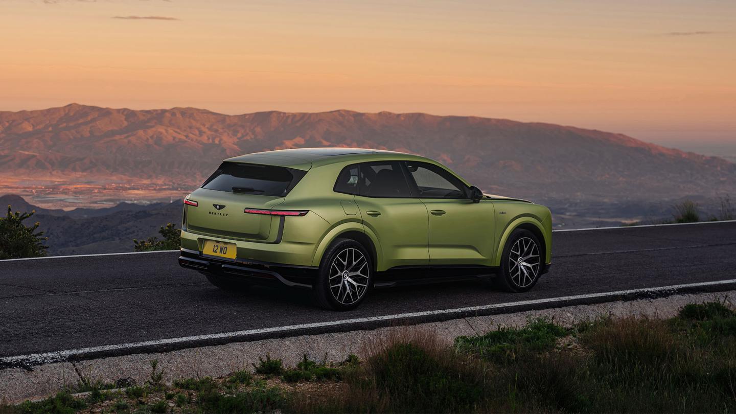 Rear three-quarter view of the Bentley Torcal S in Electrum Satin driving on the road.