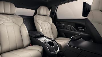 Bentey Bentayga EWB Mulliner interior view for rear passenger seats featuring Mulliner emblem, with Linen hide and Blind stitching with champagne glasses in view.