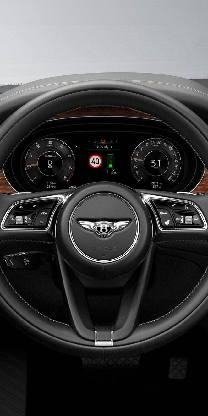 Close up of Steering wheel of Bentley Bentayga's single tone, hide trimmed, three spoke steering wheel with digital dashboard in view.