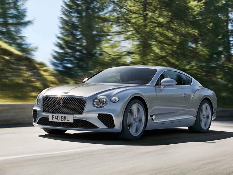 Bentley Continental GT V8 model in Moonbeam colour featuring Black gloss matrix grille with chrome surround, driving with greenery in backdrop.