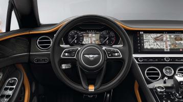 Driver side view of Bentley Continental GT Speed with steering wheel in view featuring High Gloss Carbon Fibre veneer and Mandarin by Mulliner hide. 