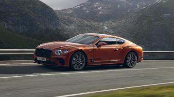 Bentley Continental GT Speed W12 in Orange Flame featuring Dark tint radiator matrix driving along a highway with mountains in backdrop.