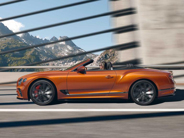Side view of Bentley Continental GTC Speed in Orange Flame with roof down driving on a highway.