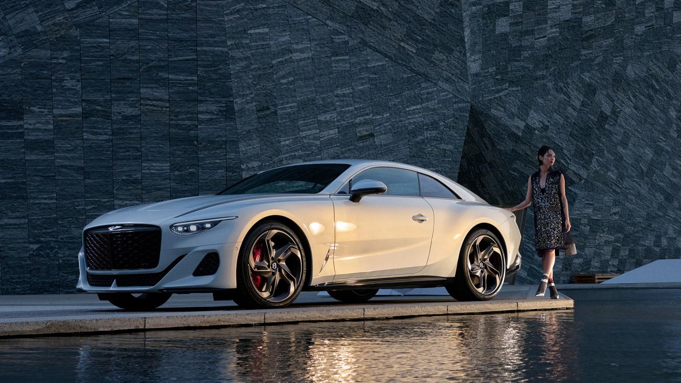Bentley Batur by Mulliner in White, side view featuring 22" 5 spoke directional alloy wheel – black painted with a female/person/ model posing at rear end.