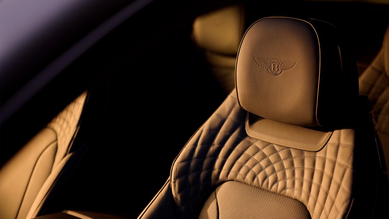 Bentley front seat seen through the open side window with light shining on it.