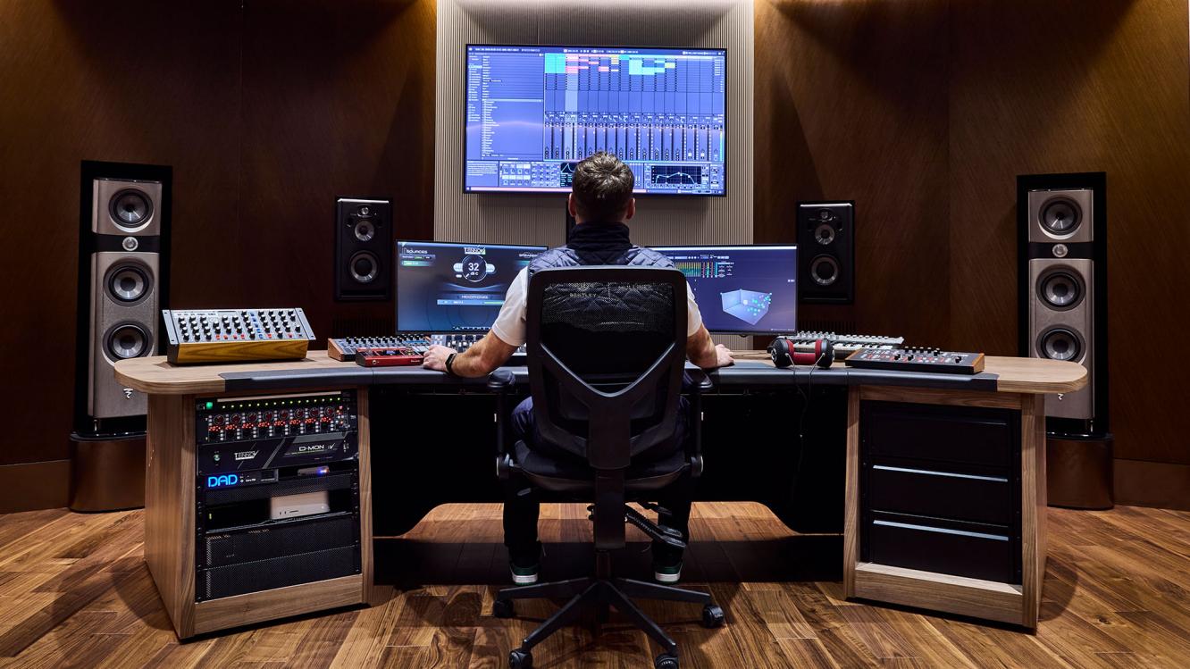 Audio engineer wearing a Bentley Mulliner jacket sat at a desk with audio consoles, screens and speakers.