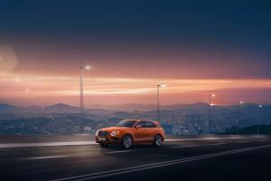 Front side angled view of Bentley Bentayga Speed in Orange Flame colour featuring Matt black matrix grille and 22 inch Alloy wheels driving along a highway.