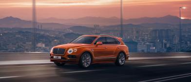 Front side angled view of Bentley Bentayga Speed in Orange Flame colour featuring Matt black matrix grille and 22 inch Alloy wheels driving along a highway.