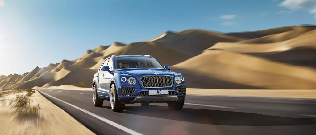 Bentley Bentayga EWB in Kingfisher colour featuring Bright chromed matrix style grille to lower bumper apertures, and Bentley Wing badge to bonnet, driving along a desert highway.