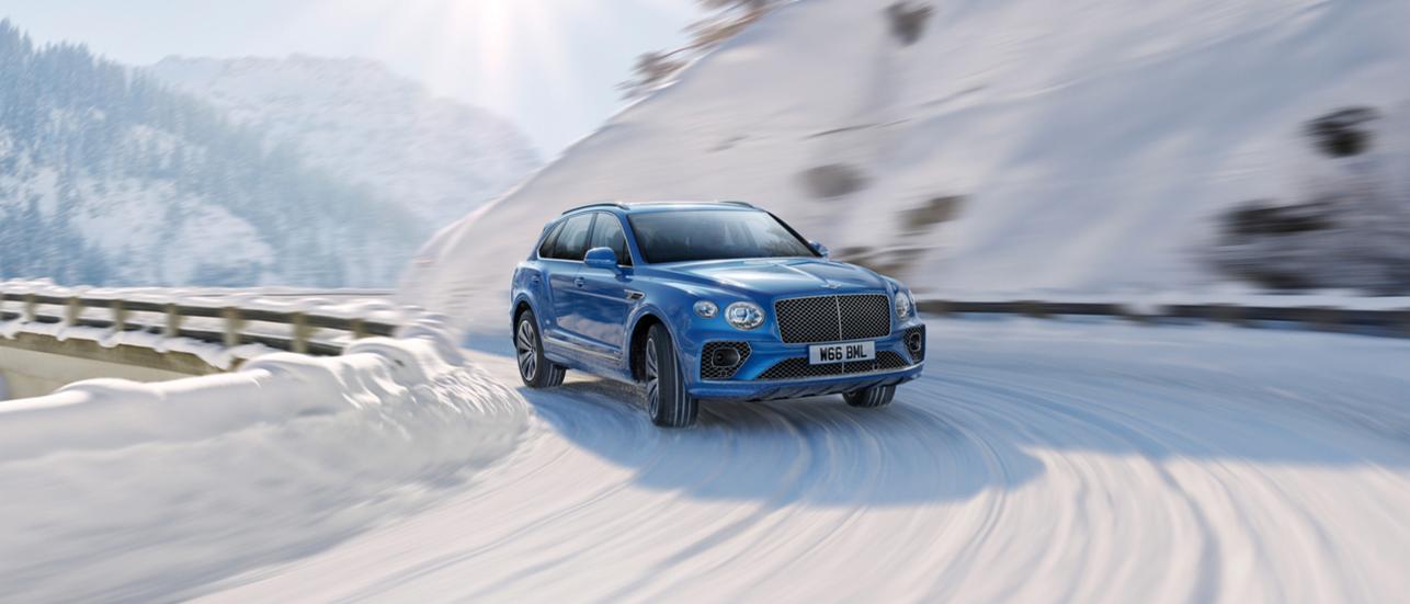 Front three quarte view of Bentley Bentayga effortlessly driving along icy road.