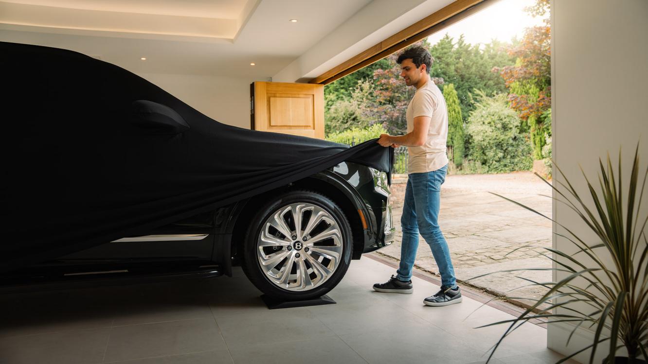 A Bentley customer uncovering his Bentayga from underneath an indoor car cover